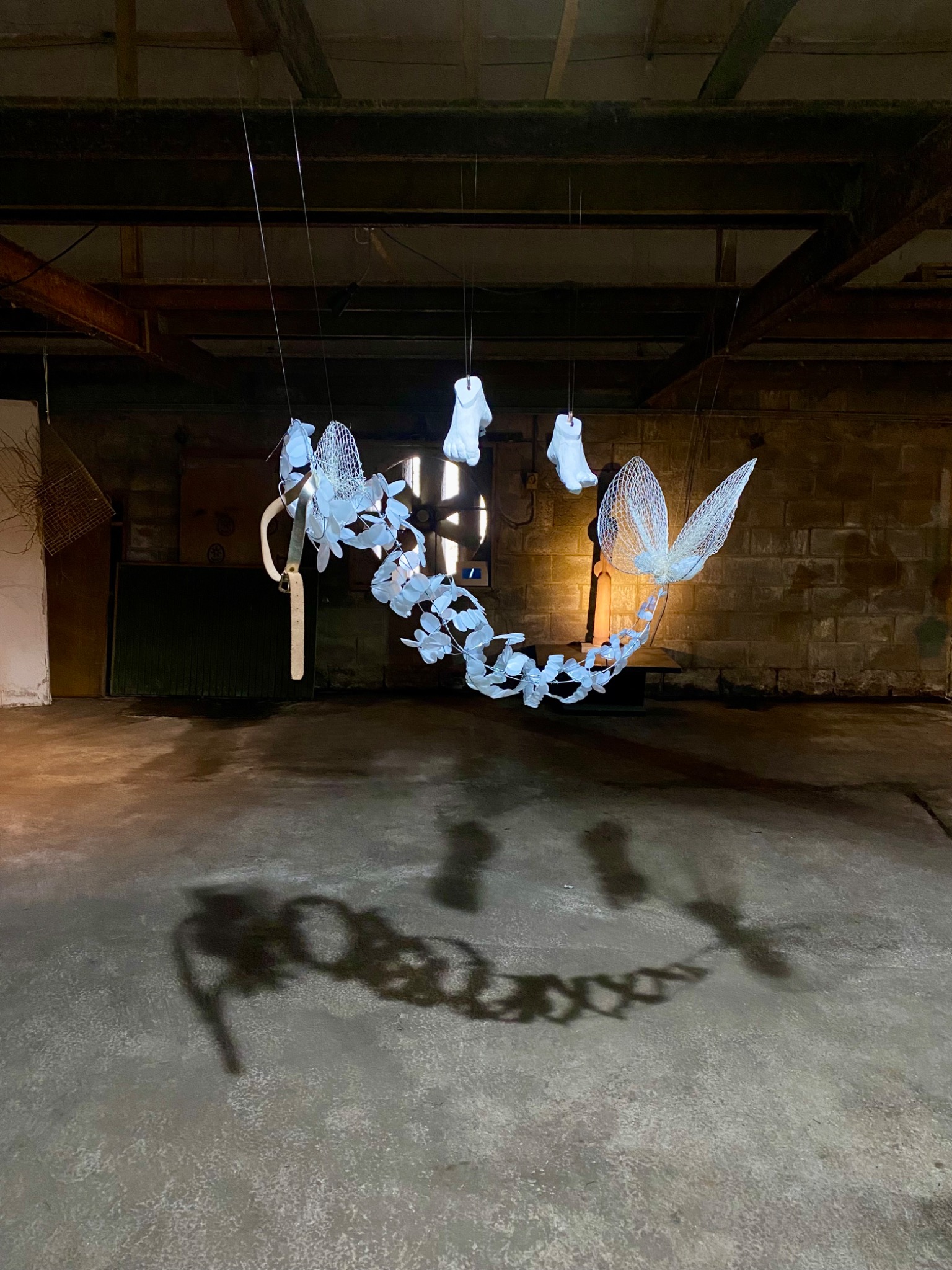 Hanging chain of translucent forms with three small cast feet; strong shadows on concrete floor.