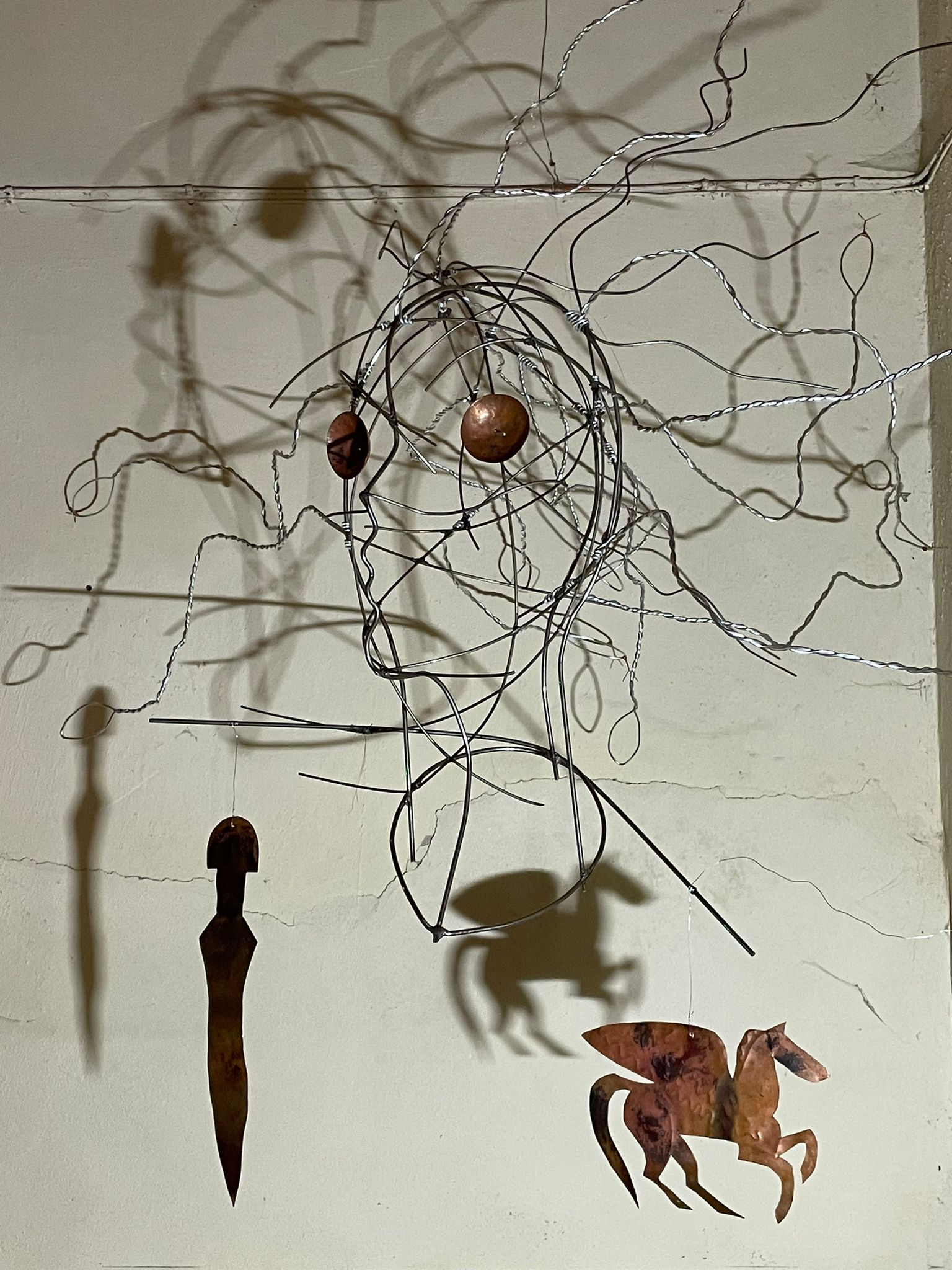 Hanging wire head with copper Pegasus and dagger casting shadows on wall.